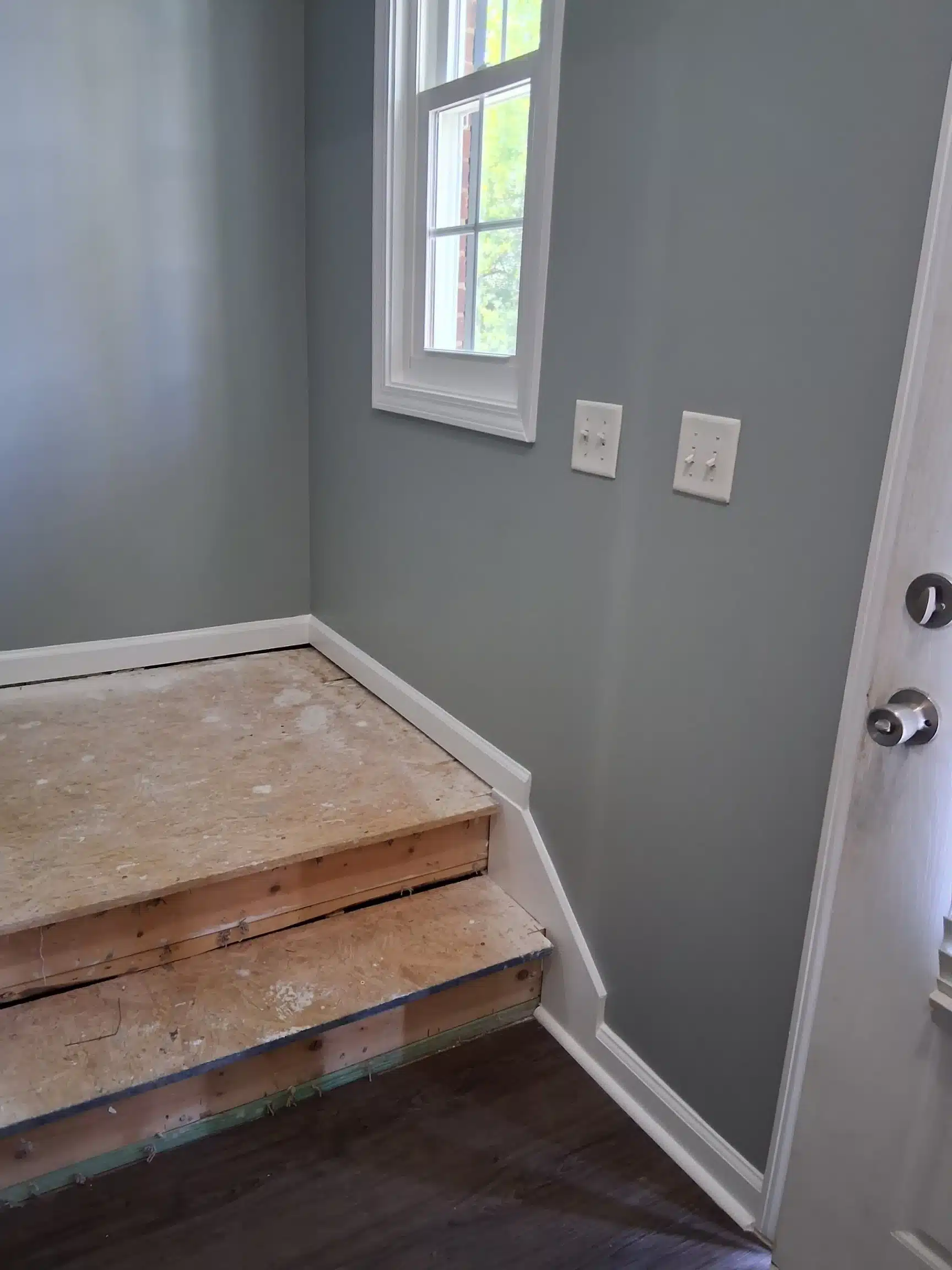 Landing with the carpet and pad lifted, exposing the subfloor and stair nosing beside the entry door