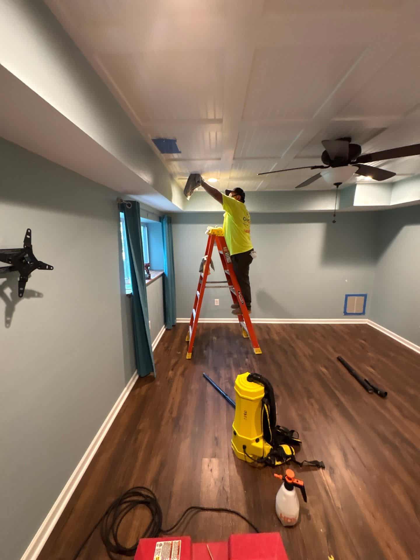 A One Stop Restoration technician on a ladder repairing a ceiling during a fire damage rebuild