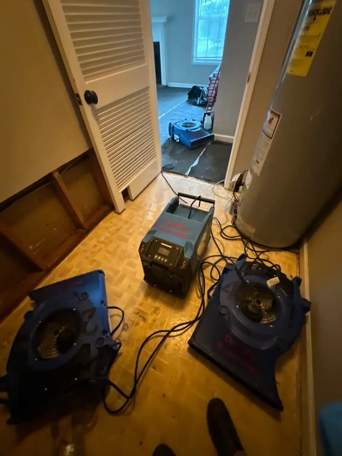 Laundry closet with the flooring removed and air movers running against the exposed subfloor