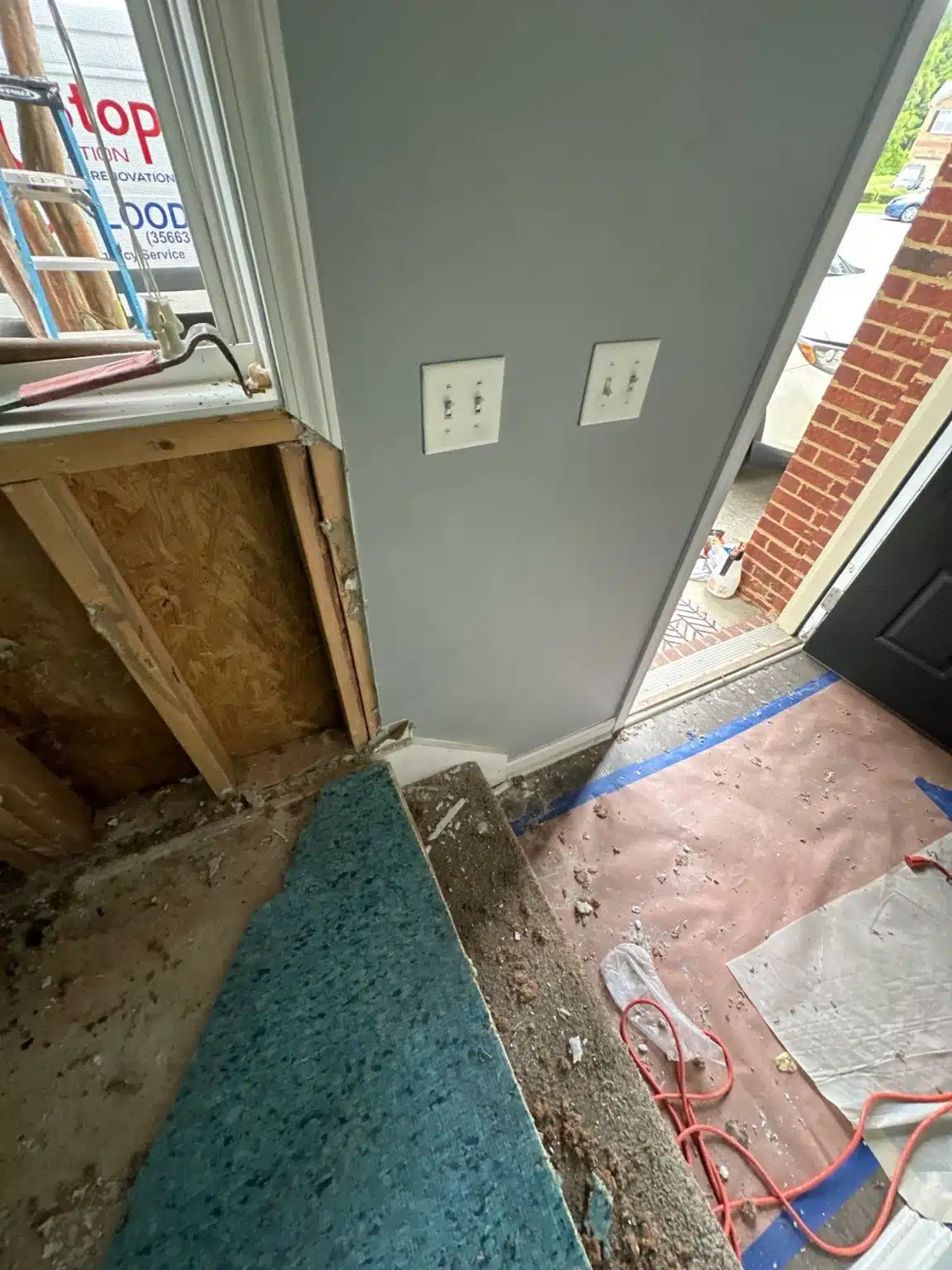 Flooring stripped back to the subfloor at the entry, with the affected wall opened to the framing