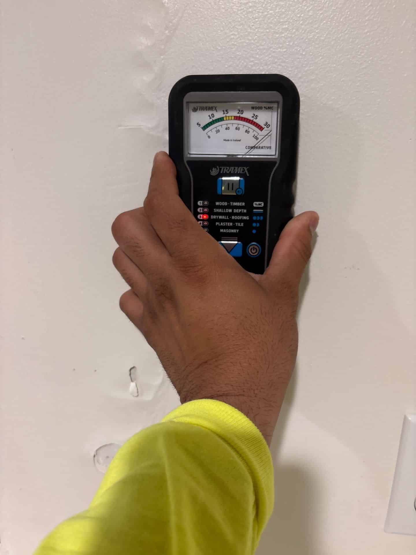 A moisture meter being held against a wall to define the true boundary of a mold problem