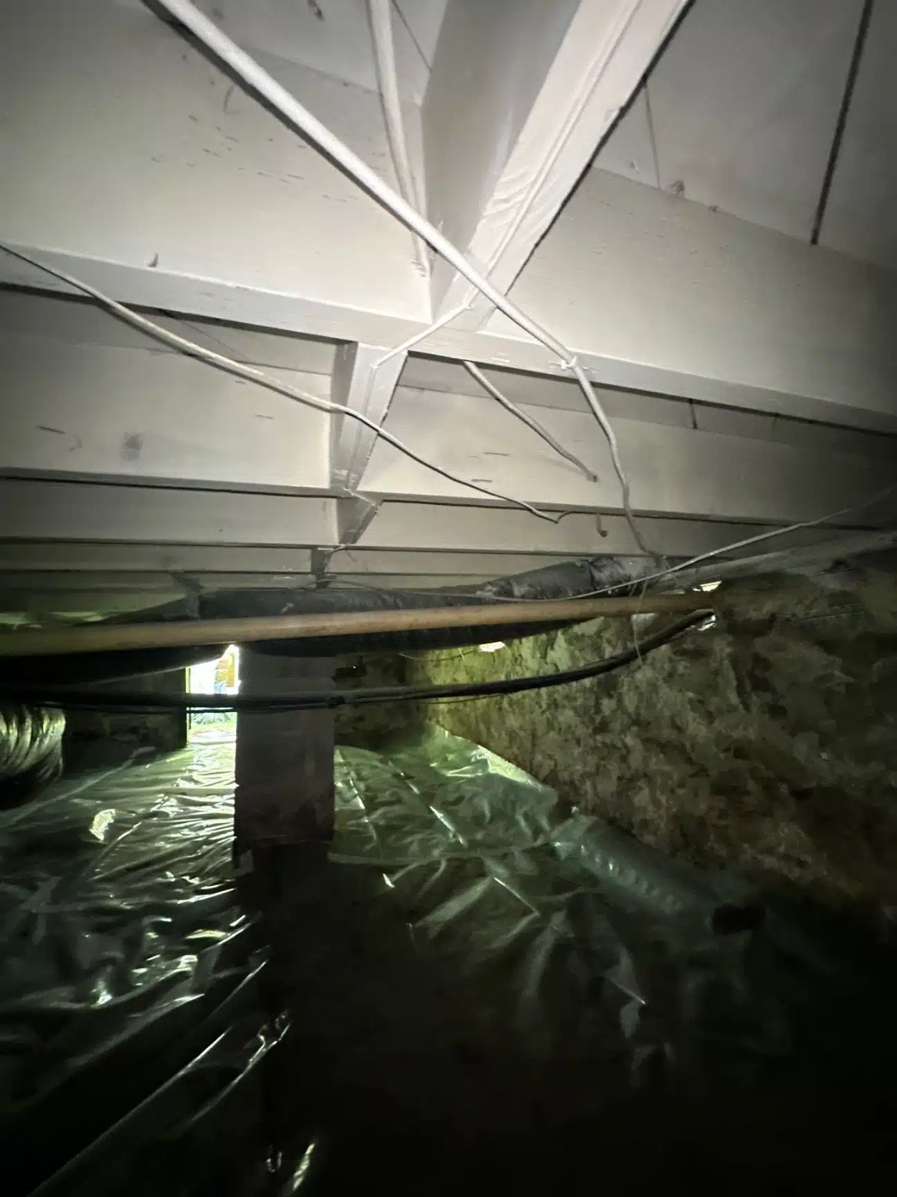 Standing moisture across the crawlspace dirt floor beneath the floor joists