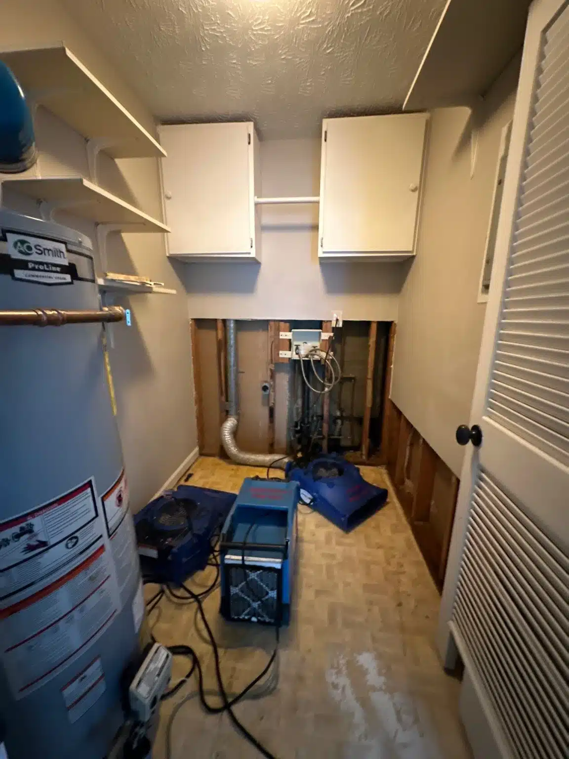 Laundry closet with water heater and shelving, drying equipment set against the opened floor