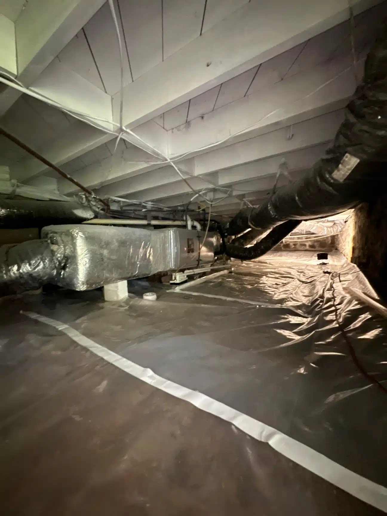 Ductwork and insulated lines running through the damp crawlspace before remediation
