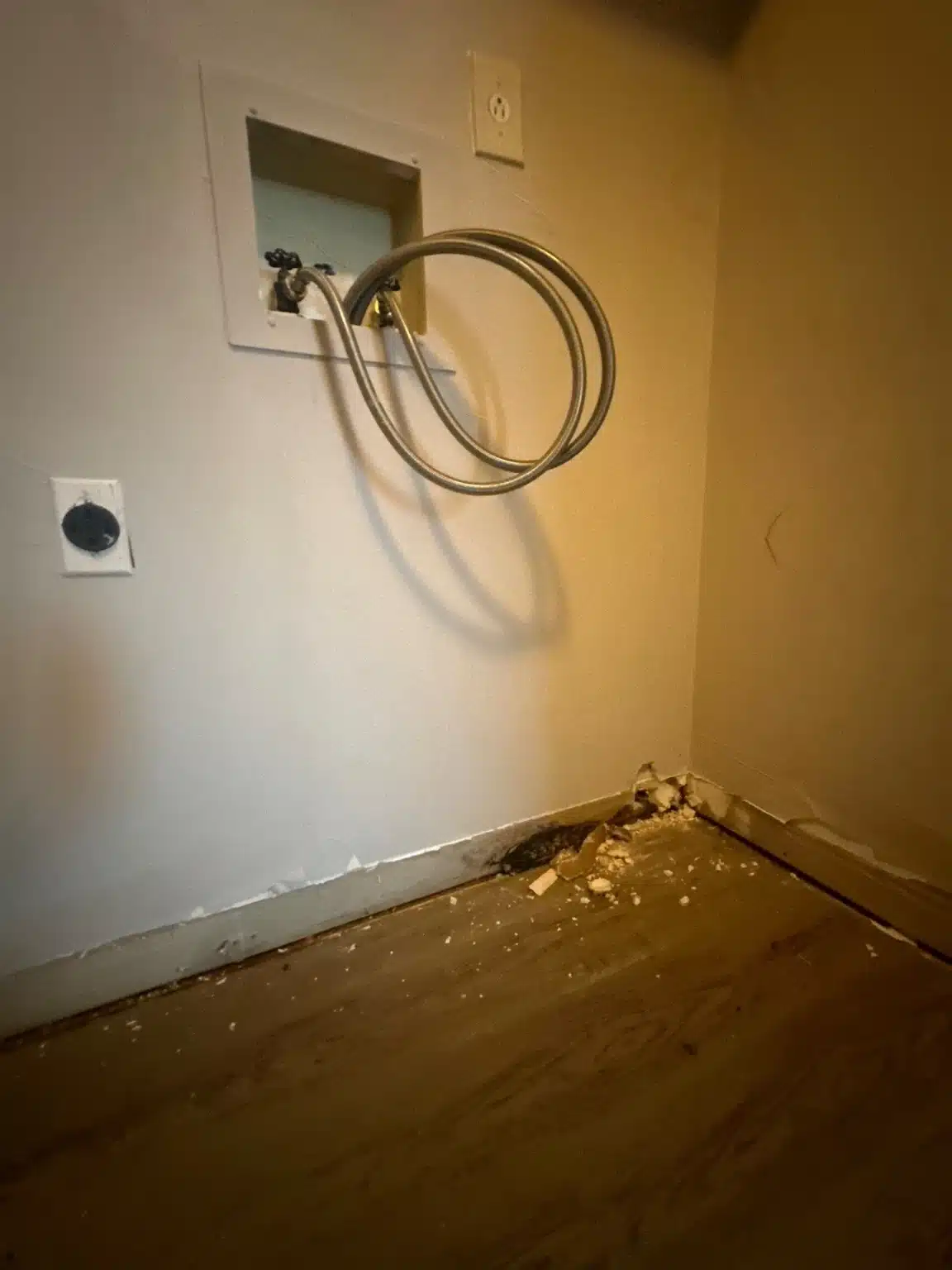 Washer hookup box and supply hoses above the affected flooring, with the baseboard removed