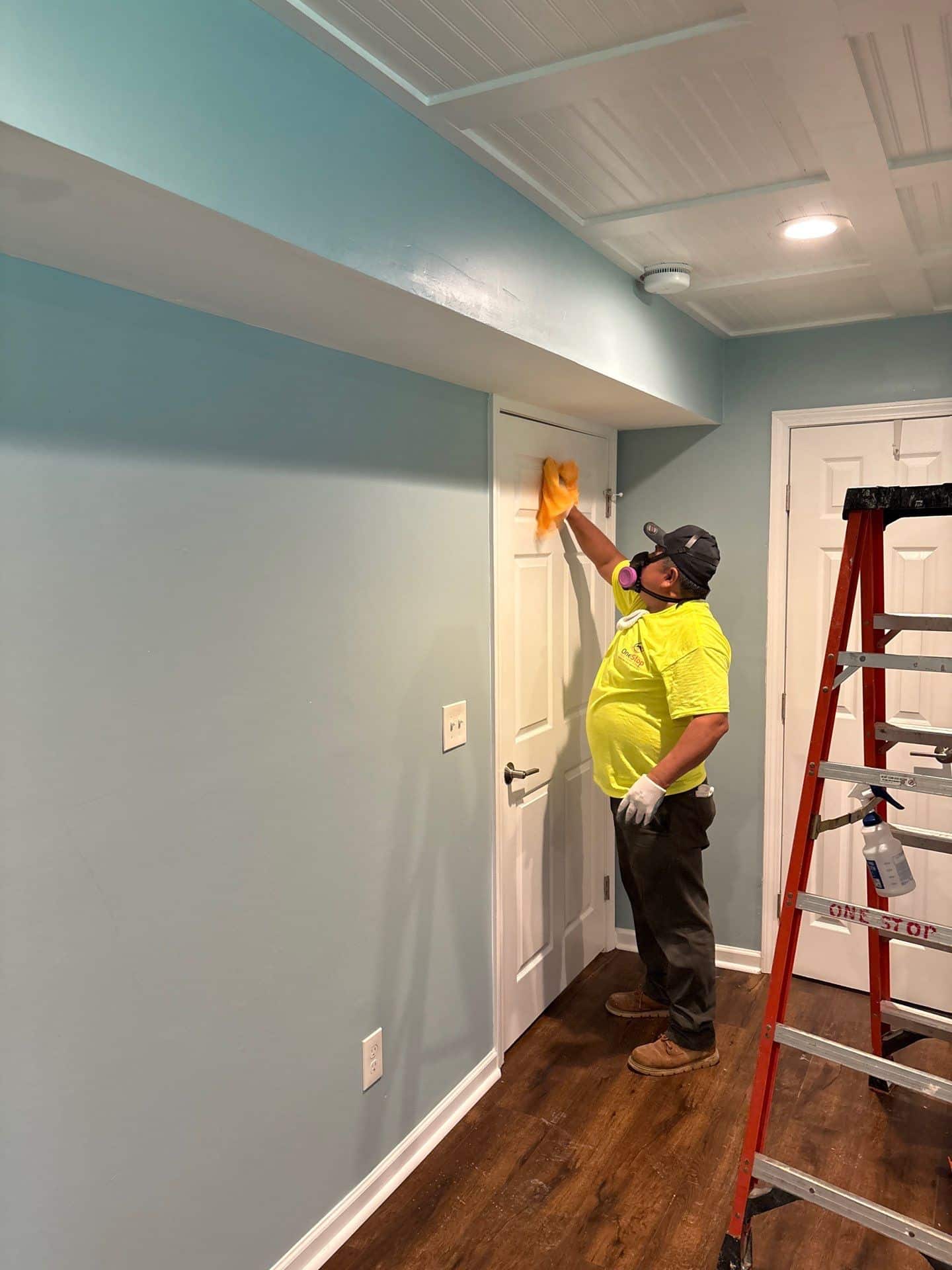 A One Stop Restoration crew member on a ladder finishing a ceiling during reconstruction after a water loss