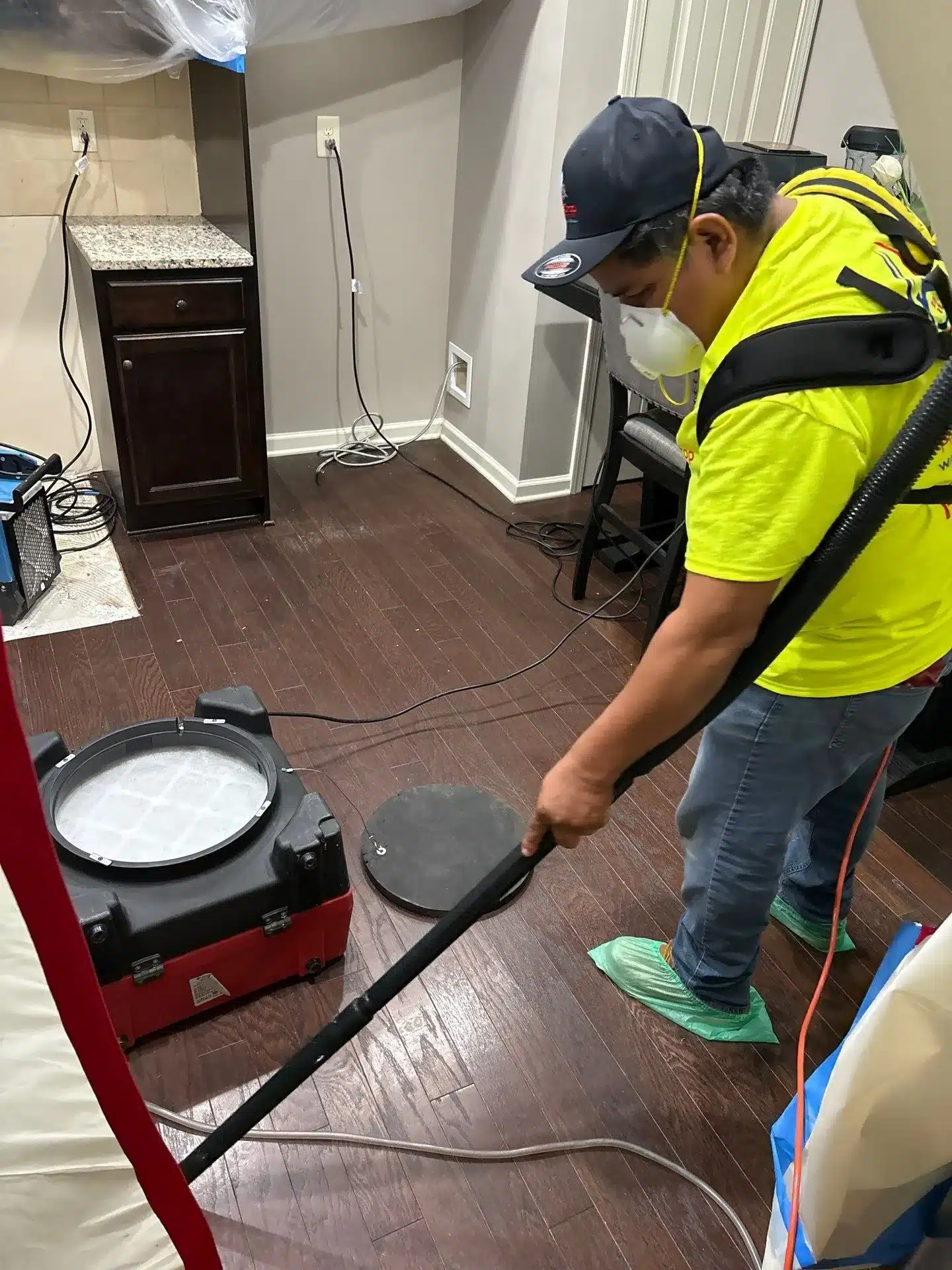 Worker in safety vest operating water extraction equipment on dark wood flooring indoors