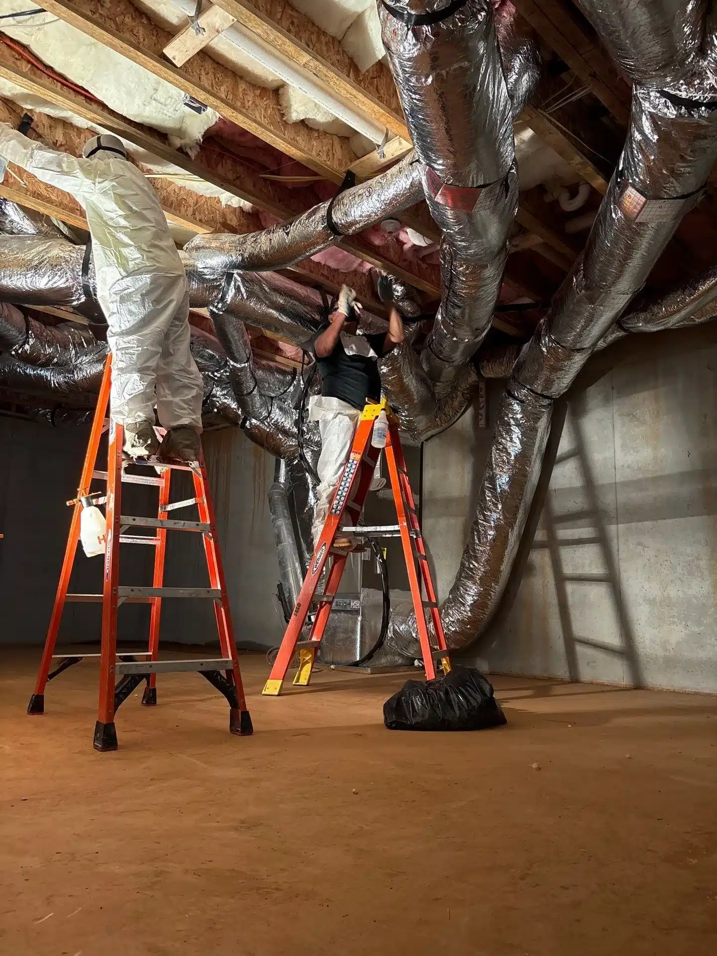 Technician on ladders reinstalling wrapped ductwork between exposed joists during a restoration job