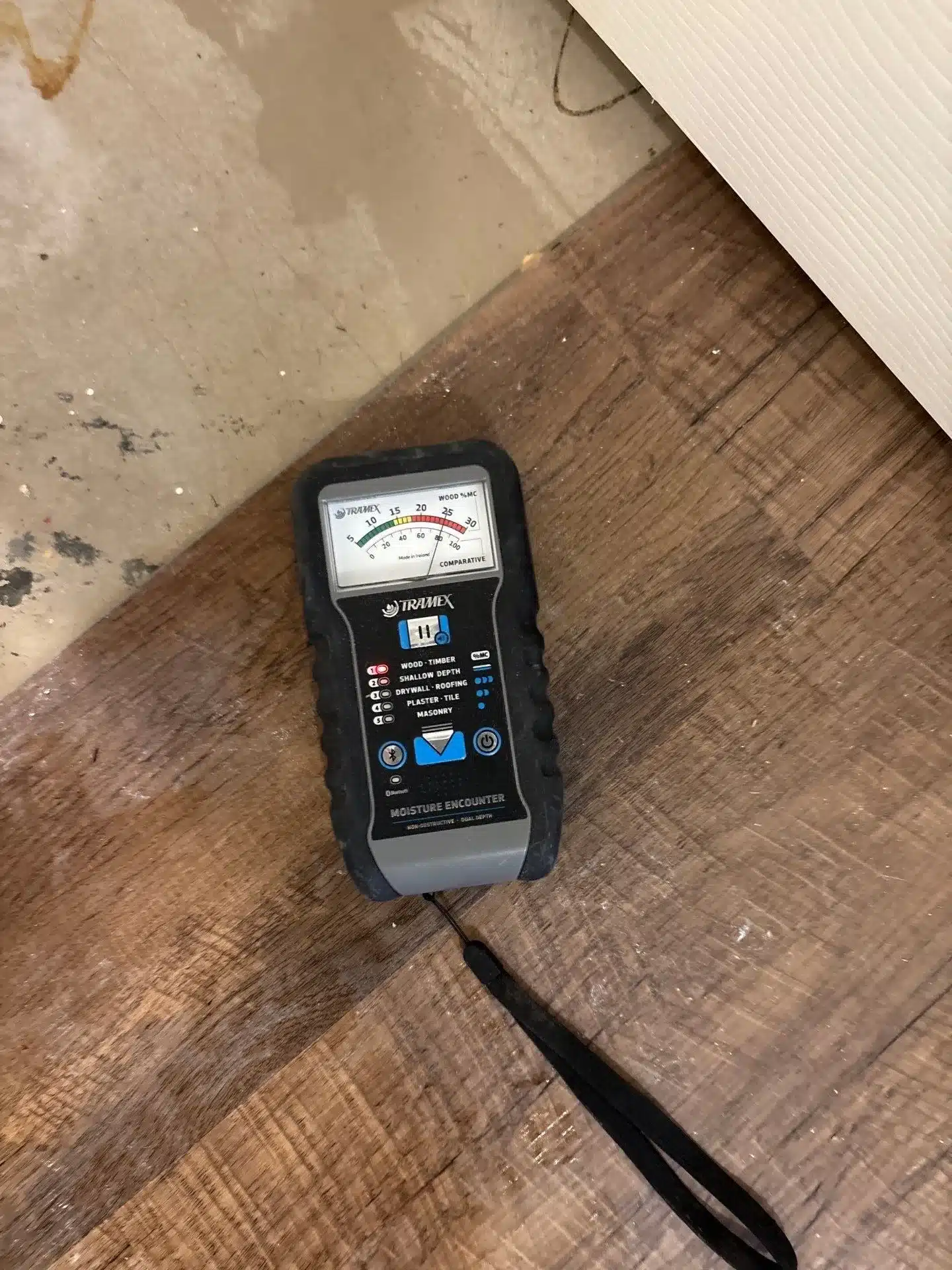 Moisture meter on wood-look flooring beside exposed subfloor during moisture assessment